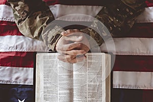 American soldier mourning and praying with the American flag and the Bible in front of him