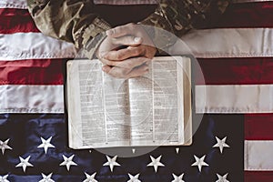 American soldier mourning and praying with the American flag and the Bible in front of him