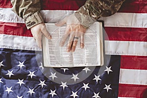 American soldier mourning and praying with the Bible in his hands and the American flag