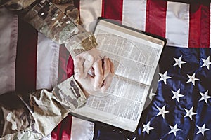 American soldier mourning and praying with the Bible in his hands and the American flag