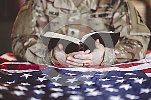 American soldier mourning and praying with the Bible in his hands and the American flag