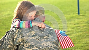 American soldier reunited with daughter on a sunny day outdoor.