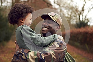 American Soldier In Uniform Returning Home On Leave To Family Carrying Daughter In Arms