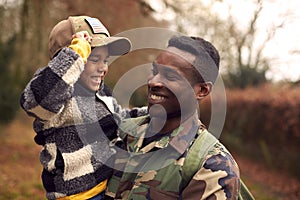 American Soldier In Uniform Returning Home To Family On Leave With Son Wearing Army Cap