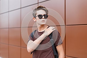 American stylish hipster young man in a brown stylish t-shirt in dark sunglasses with a trendy hairstyle with