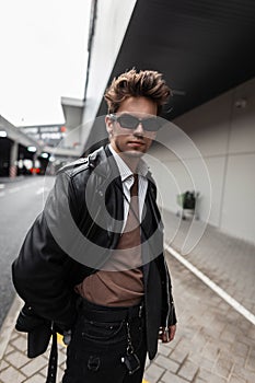 American trendy young man hipster in sunglasses in a youth oversized fashionable black leather jacket with a stylish hairstyle