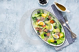 American version of Nicoise salad with canned tuna, boiled potatoes and green asparagus beans in an oval white dish on a gray