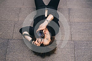 American woman photographer with digital camera is lying on the steps. Top view