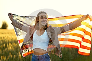 American woman proudly holding American flag at sunset field, celebrate 4th of July