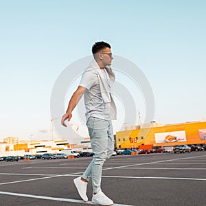 American young model man in sunglasses in vintage blue jeans in a stylish white T-shirt in sneakers walks around the city. Urban