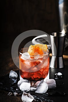 Americano Alcohol cocktail with red vermouth, bitter, soda, orange zest and ice, dark wooden bar counter background, bar tools,