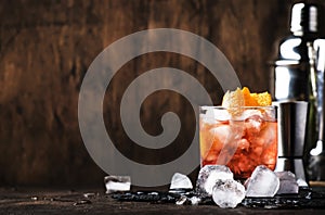 Americano Alcohol cocktail with red vermouth, bitter, soda, orange zest and ice, dark wooden bar counter background, bar tools,