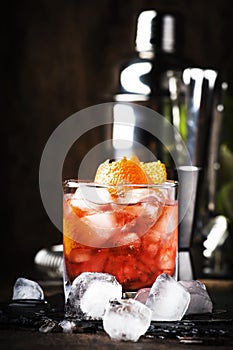 Americano Alcohol cocktail with red vermouth, bitter, soda, orange zest and ice, dark wooden bar counter background, bar tools,