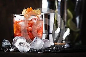 Americano Alcohol cocktail with red vermouth, bitter, soda, orange zest and ice, dark wooden bar counter background, bar tools,