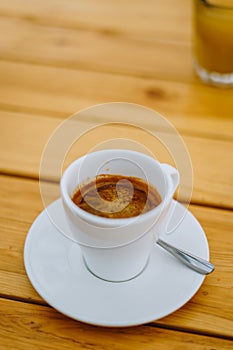 Americano in a white cup on a wooden table. Delicious morning coffee in a summer cafe. White cup with coffee on a plate