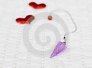 Amethyst crystal quartz pendulum and two red hearts on white cloth.Valentine`s concept