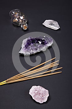 Amethyst and quartz crystal stones, aromatic sticks and decorative bottle on black background