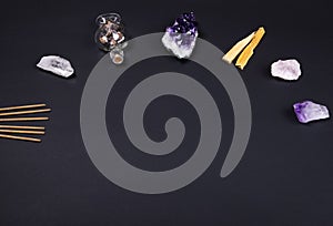 Amethyst and quartz crystal stones, palo santo wood, aromatic sticks and decorative bottle on black background