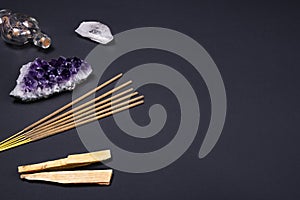 Amethyst and quartz crystal stones, palo santo wood, Aromatic sticks and decorative bottle on black background.