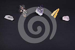 Amethyst and quartz crystal stones, palo santo wood and decorative bottle on black background.