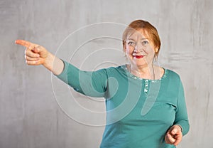 Amiable elderly woman in teal jumper pointing towards