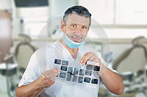 Amiable male dentist surgeon in white uniform showing dental X-rays