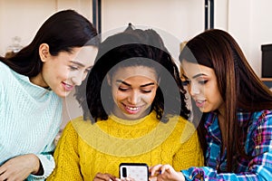 Amiable multiracial girls browsing social media using smartphone at home