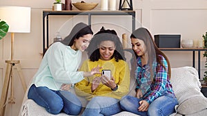 Amiable multiracial girls browsing social media using smartphone at home