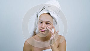 Amiable teenager wrapped in towels examining her face with acne