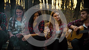 Amiable tourists by campfire singing songs with guitar in dark forest