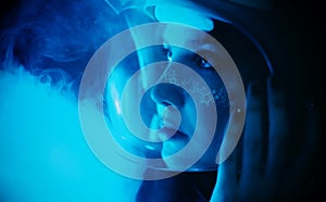 Amidst the dark of night and mist, a young woman in an astronaut helmet, adorned with starry makeup illuminated by the blue light