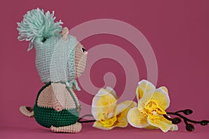 Amigurumi kitten doll on pink background next to yellow orchid flowers. A soft DIY toy made of cotton. One brown cat