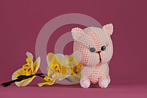 Soft DIY toy made of natural cotton and wool. Cute little crocheted cat, handmade art. Amigurumi kitten doll on pink