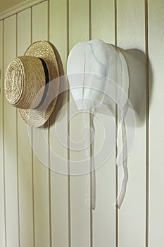 Amish bonnet and straw hat hanging on wall