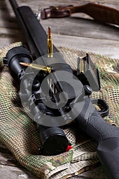 The Ammo with black bolt action rifle and scope on the multicam background. Close up