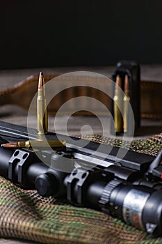The Ammo with black bolt action rifle and scope on the multicam background. Close up
