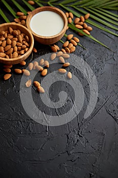 Amond seeds in wooden bowl, fresh natural milk placed on black stone background