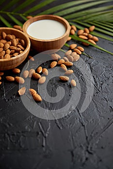 Amond seeds in wooden bowl, fresh natural milk placed on black stone background