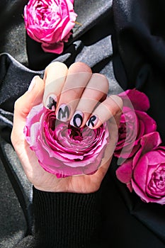 AMOR word on nails manicure hold Pink rose flower on black silk fabric. Minimal flat lay nature. Female hand. Love