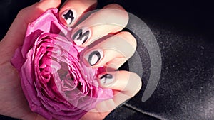 AMOR word on nails manicure hold Pink rose flower on black silk fabric. Minimal flat lay nature. Female hand. Love