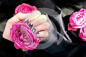 AMOR word on nails manicure hold Pink rose flower on black silk fabric. Minimal flat lay nature. Female hand. Love