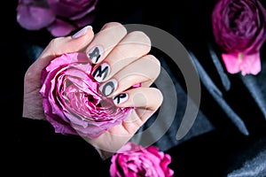 AMOR word on nails manicure hold Pink rose flower on black silk fabric. Minimal flat lay nature. Female hand. Love