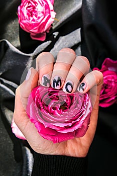 AMOR word on nails manicure hold Pink rose flower on black silk fabric. Minimal flat lay nature. Female hand. Love