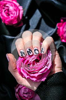 AMOR word on nails manicure hold Pink rose flower on black silk fabric. Minimal flat lay nature. Female hand. Love