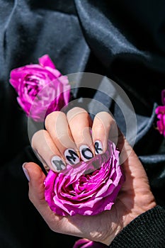 AMOR word on nails manicure hold Pink rose flower on black silk fabric. Minimal flat lay nature. Female hand. Love