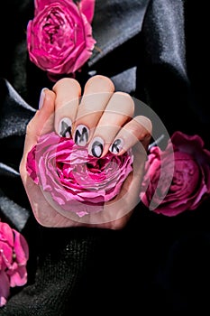 AMOR word on nails manicure hold Pink rose flower on black silk fabric. Minimal flat lay nature. Female hand. Love