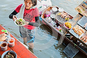 Amphawa, Thailand: a girl serves a plate with squid rings, standing in the water with her boat behind at Amphawa Floating Market