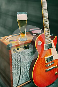 Amplifier for guitar with guitar, glass of beer and notepad on black background. Gently toned
