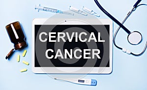 Ampoules, pills, stethoscope, thermometer, tablet with CERVICAL CANCER text on desktop.