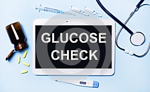 Ampoules, pills, stethoscope, thermometer, tablet with GLUCOSE CHECK text on desktop.